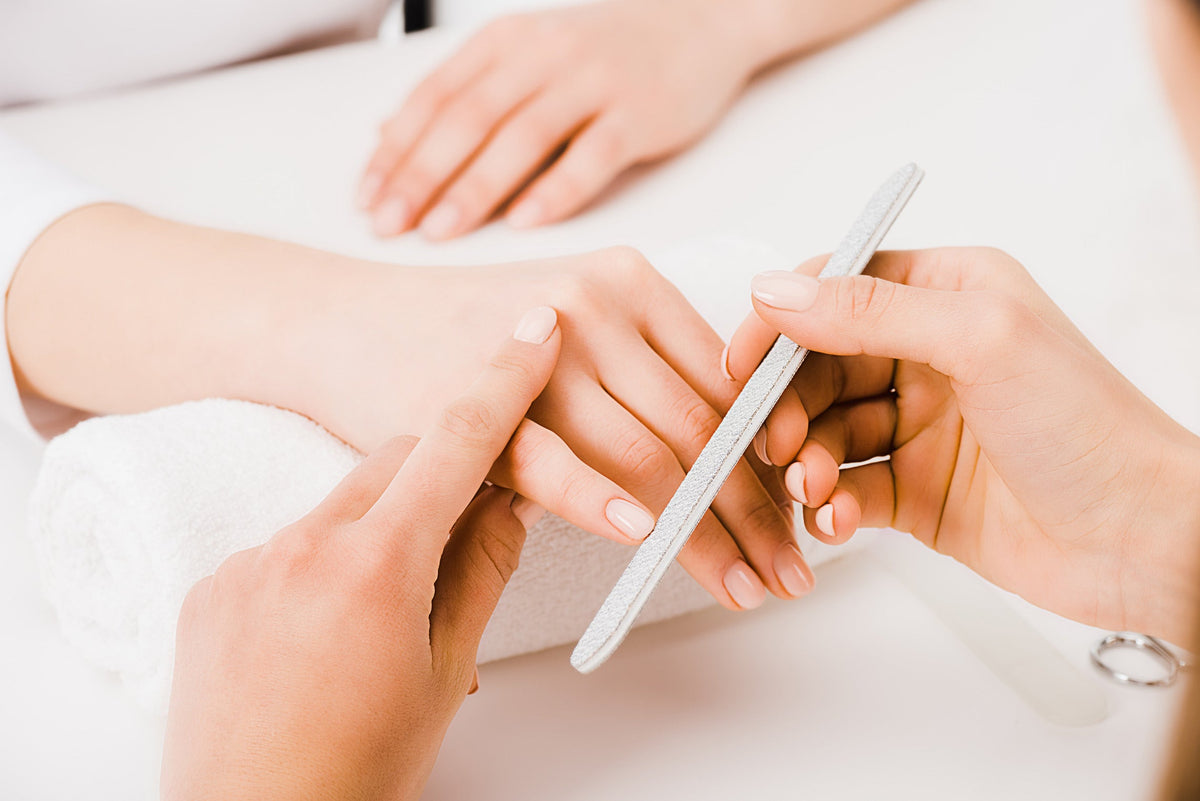 Nagelstyliste gebruikt een nagelvijl tijdens een manicure