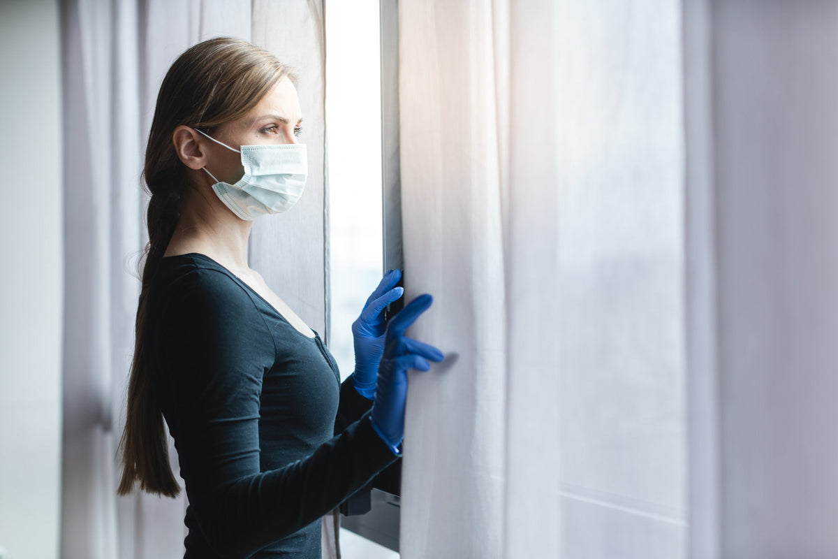 Nail technician with a mask and gloves looking out a window