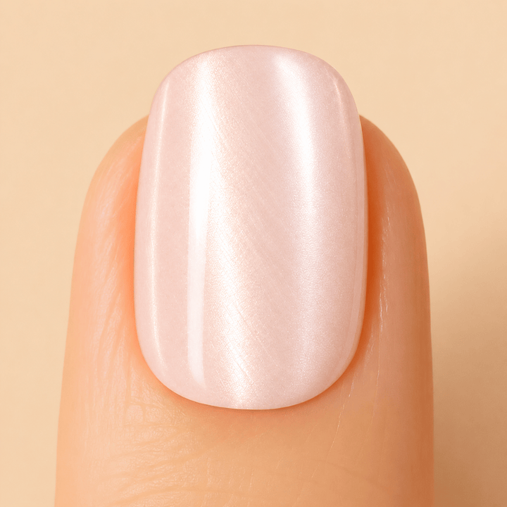A close-up of a fingernail with a glossy, champagne manicure showing a subtle pearlescent sheen,