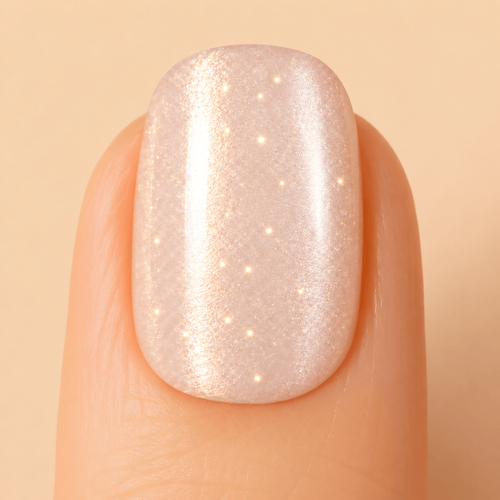 A close-up of a fingernail with a glossy, iridescent pearl shimmer nail polish in a warm champagne-pink shade.