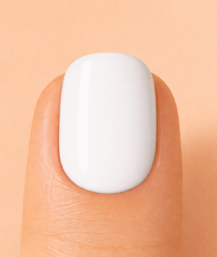 Close-up of a white nail polish on a finger against a peach background
